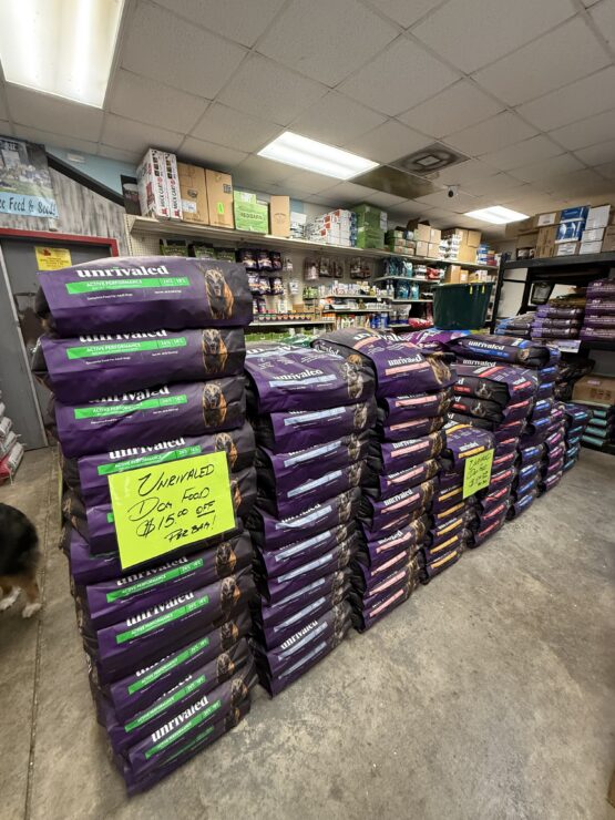 Stack of Unrivaled Bags of dog food with a sign that says "Get $15 Off Bags of Unrivaled Dog Food"